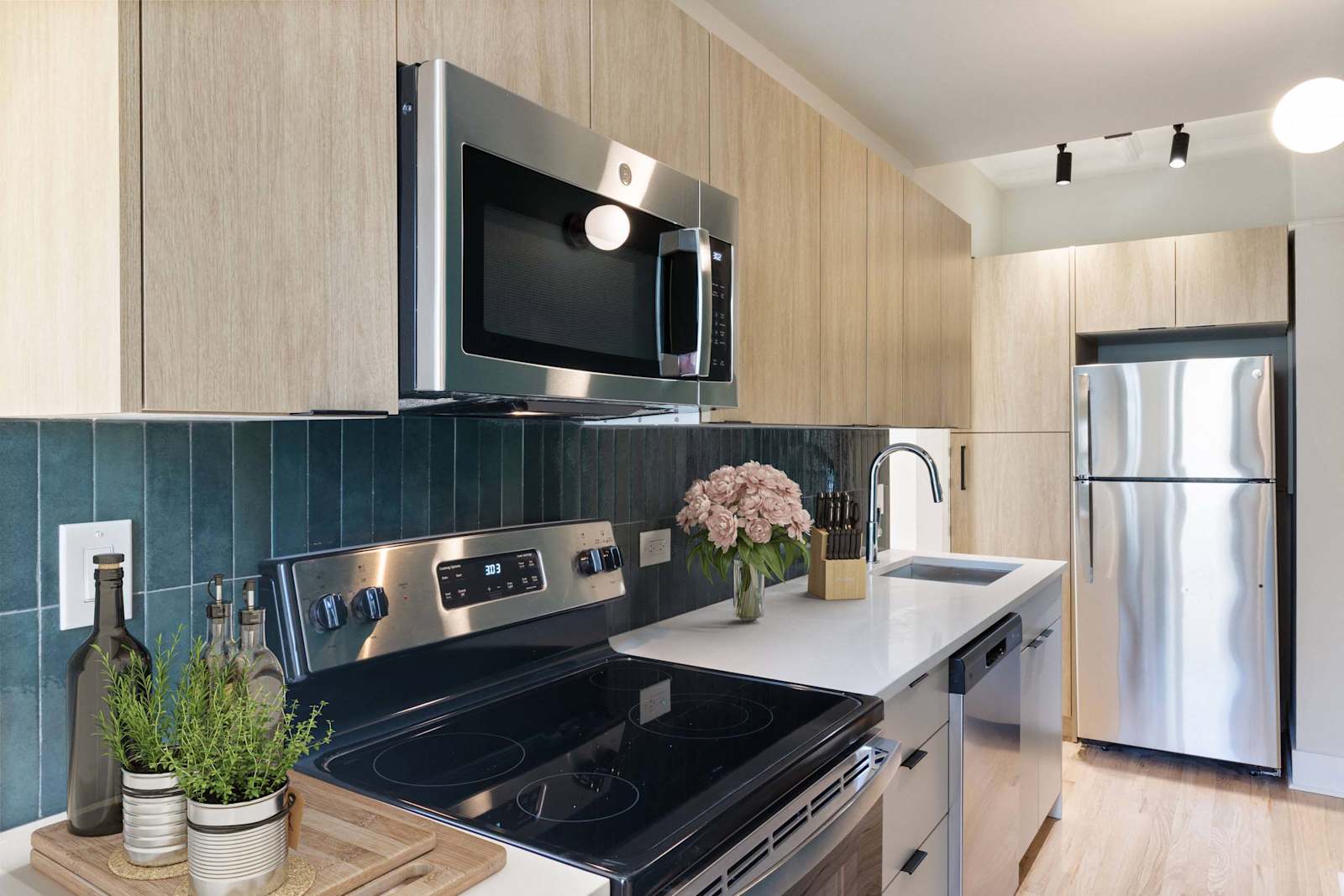 large kitchen with stainless appliances, modern cabinetry, track lighting, and wood style flooring