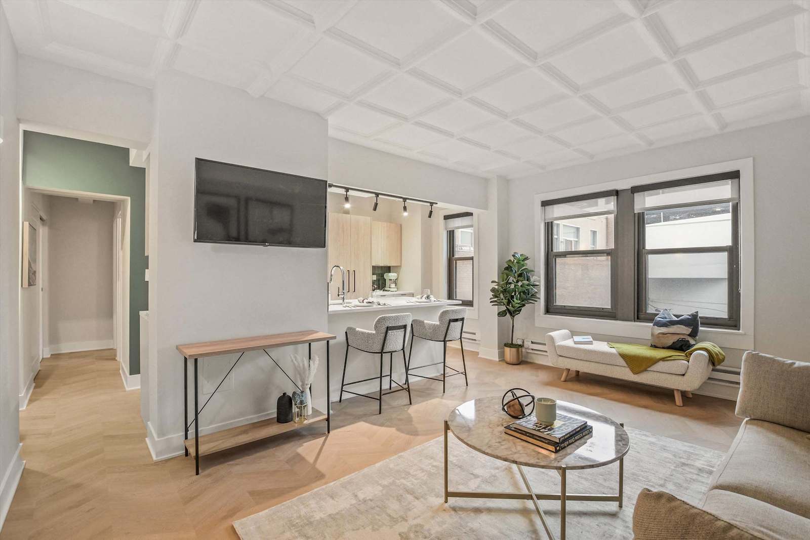 living room with coffered ceiling, light herringbone wood style flooring, and open kitchen with bar seating.